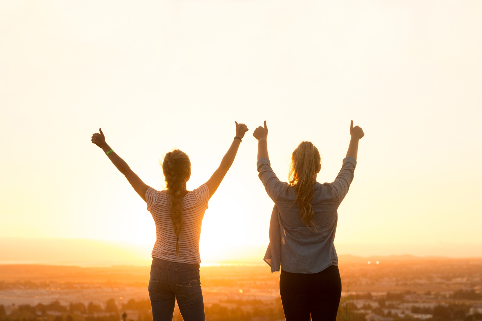 Two healthy women with thumbs up looking at the sunset