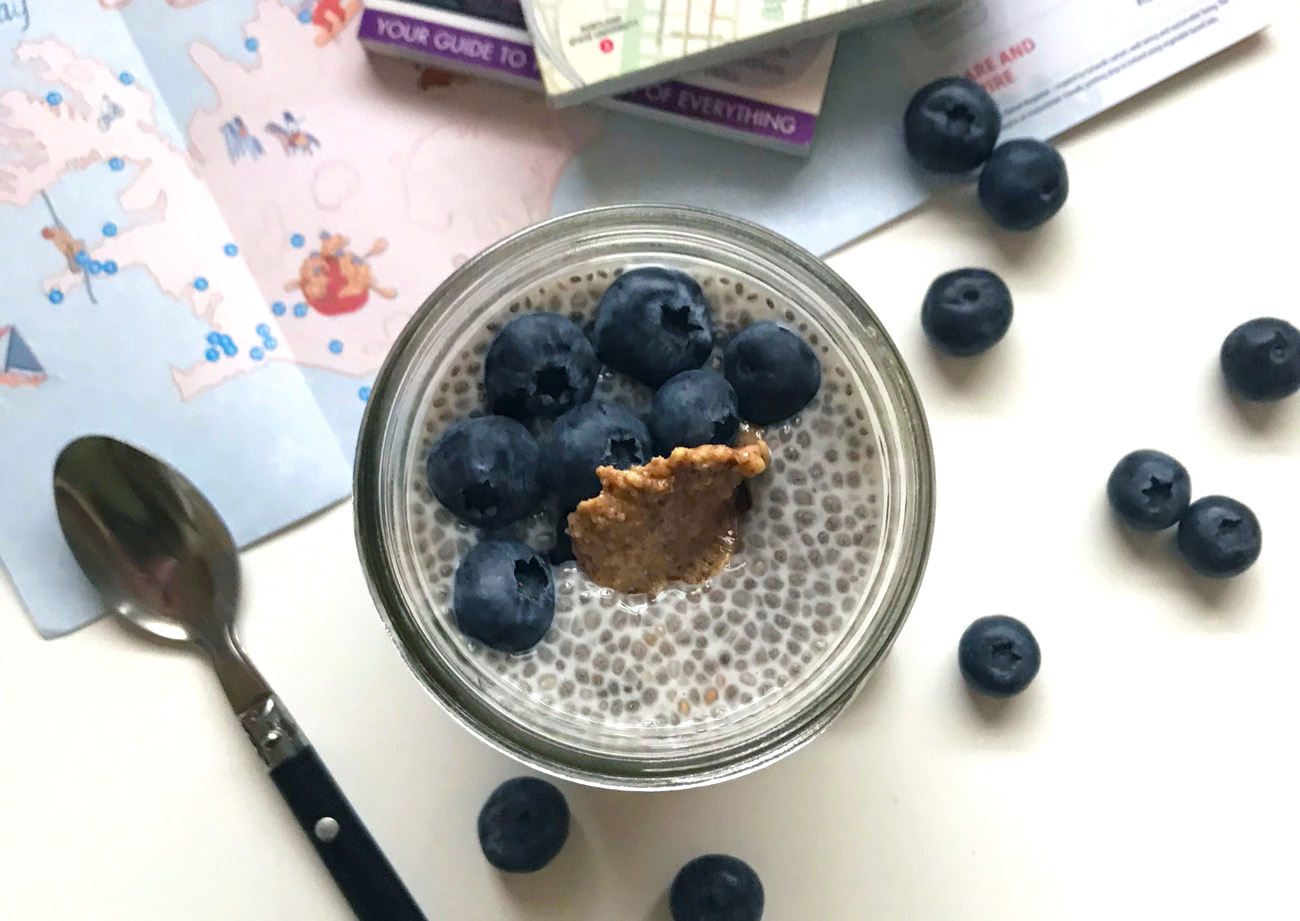 protein chia seed pudding topped with blueberries and almond butter in a mason jar surrounded by blueberries maps and a spoon